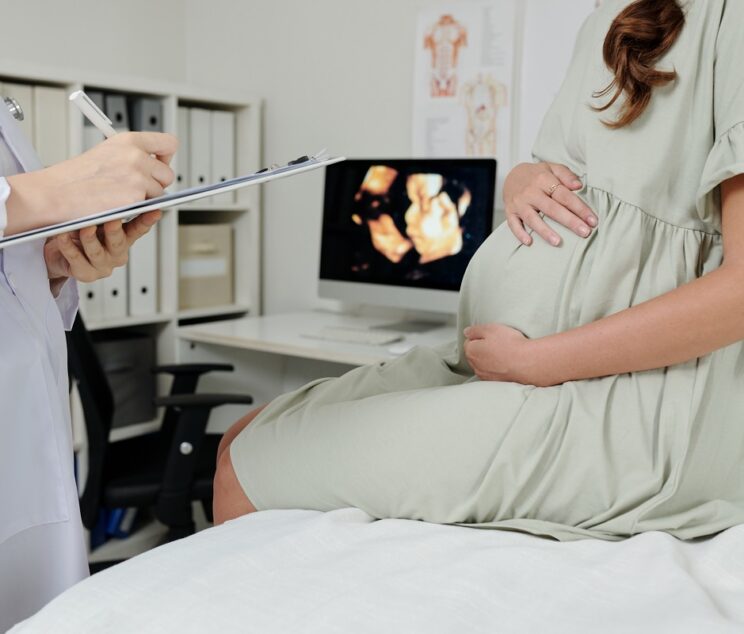 Close-up of doctor making notes in medical card after ultrasound exam of pregnant woman at hospital